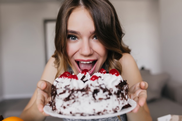 おいしいバースデーケーキでポーズをとる面白い白人の女の子 ベリーとチョコレートパイを保持している興奮した女性モデルの屋内ショット 無料の写真