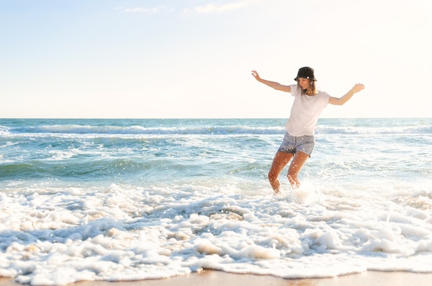 水しぶきを楽しんでいる青い海の海岸で面白い若い女性 プレミアム写真