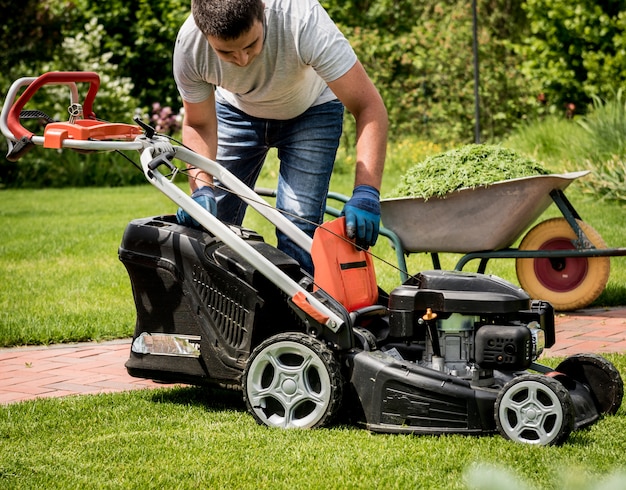 Gardener emptying lawn mower grass into a wheelbarrow ...