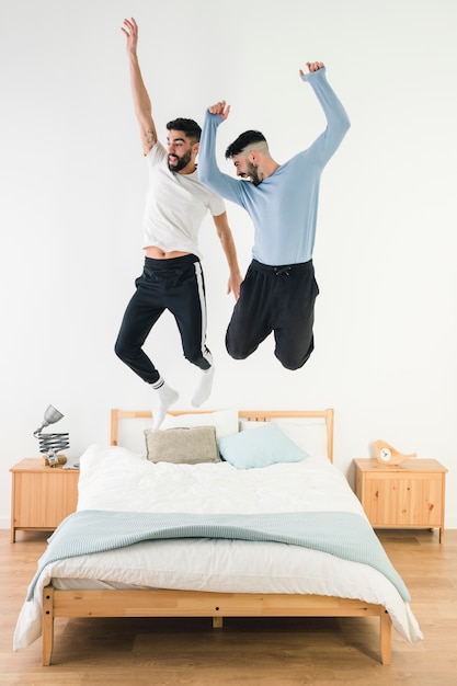 同性愛者のカップルが寝室のベッドの上をジャンプ 無料の写真