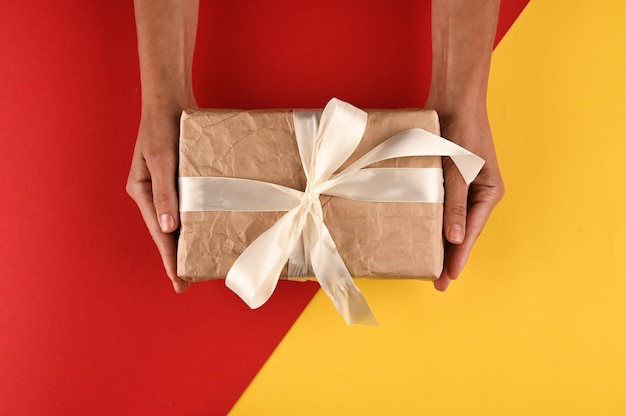 Download Premium Photo Gift Box With Bow In Female Hands On Yellow Red Background PSD Mockup Templates