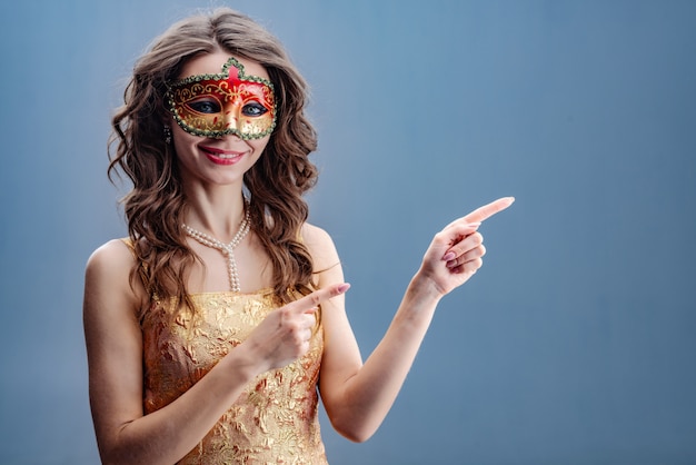 The girl in the carnival mask is smiling while standing and pointing to the side Premium Photo