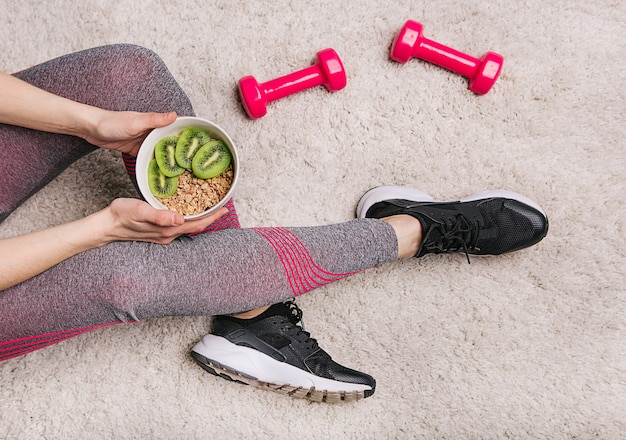 Girl holds a plate with muesli and kiwi after fitness workout with dumbbells Free Photo, strava po cvičení