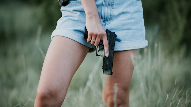 デニムのショートパンツとフィールドでポーズをとって彼の手で銃を持つ少女 閉じる プレミアム写真
