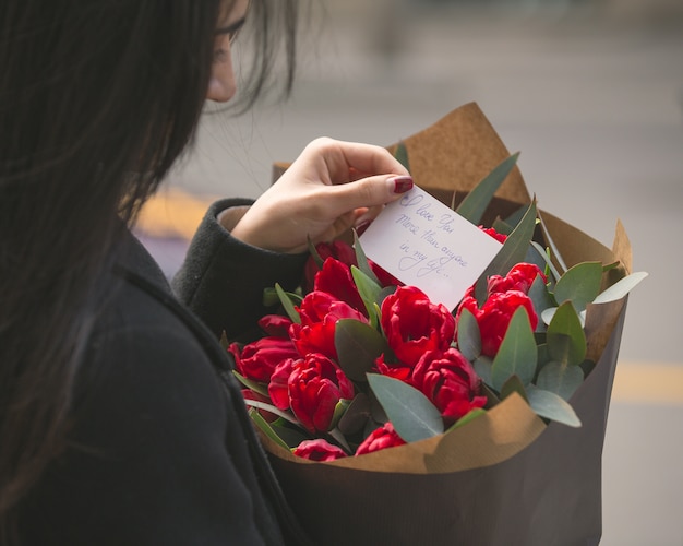 赤いチューリップの花束に入れてメモを読んでいる女の子 無料の写真