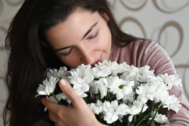 女の子は白い花の花束を嗅ぐ ブルネットの抱擁は 彼女の最愛の人から繊細な花の花束を嗅ぎます 愛する人への素敵な贈り物 プレミアム写真