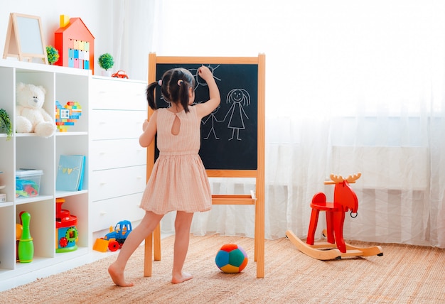 女の子は黒板で子供部屋に立って チョークで家族を描く プレミアム写真