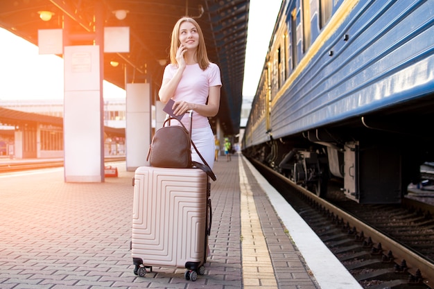 スーツケースを持って駅のホームに立っている女の子 電車を待つ 学生が旅行する 夏休みに出発 コピースペース プレミアム写真