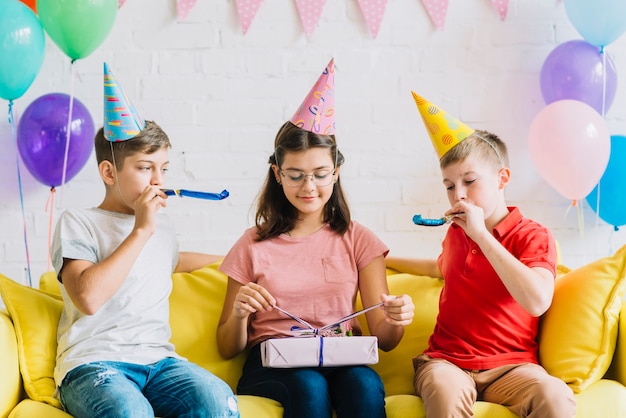 Girl Unwrapping Birthday Gift While Her Friends Blowing