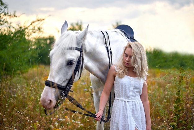 Premium Photo | Girl in white dress holding a horse in the field