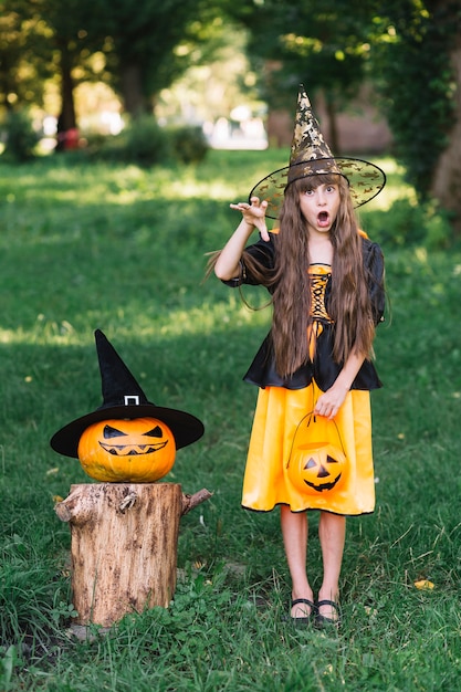 Free Photo | Girl in witch costume showing reach out hand near pumpkin