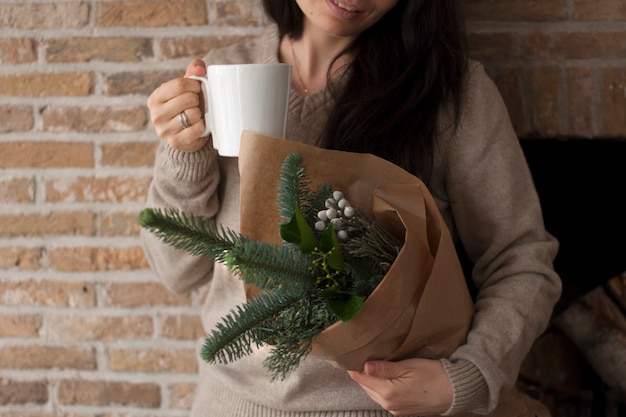 茶色の紙の手で小枝の花束を持つ少女 レンガの壁の近く 手にコーヒーのマグカップで プレミアム写真