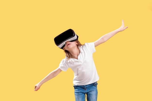 Girl y.o in formal outfit wearing vr glasses putting hands out in excitement isolated on yellow . child using a gaming gadget for virtual reality. virtual technology Premium Photo