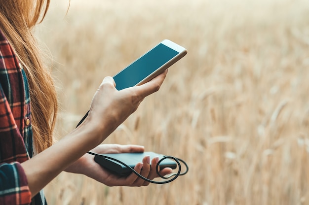 Premium Photo | Girl in a yellow field holding a phone in her hand, and charging it from power bank.