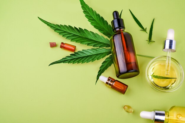 Glass bottles with cbd oil, thc tincture and hemp leaves on a yellow background. flat lay, minimalism. cosmetics cbd hemp oil. Premium Photo