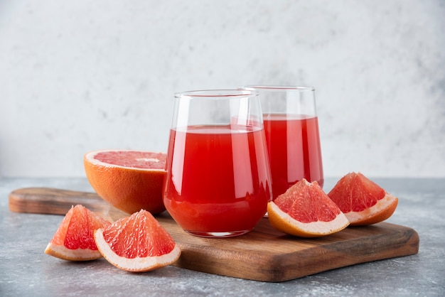 Glass cups of fresh grapefruit juice with slices of fruits placed on wooden board . Free Photo