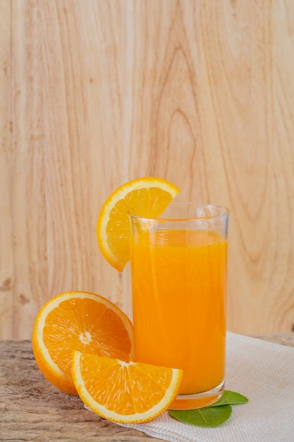 オレンジジュースのグラスを木の上に置きます 無料の写真