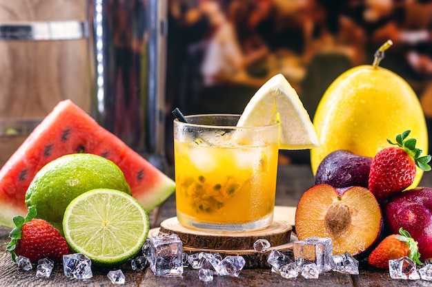 カイピリーニャ パッションフルーツ 蒸留アルコール カシャーサ 砂糖と呼ばれる典型的なブラジルの飲み物のグラス 周りの様々な果物 プレミアム写真