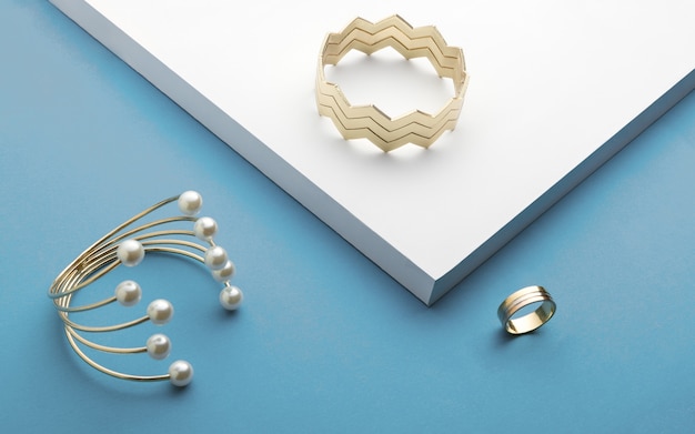 Golden bracelets and golden ring on white and blue background - zigzag bracelet and pearl golden bracelet Premium Photo