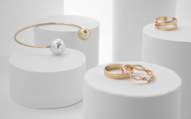  Golden pearl bracelet and rings on white paper cylinders Premium Photo