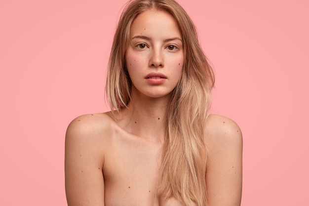 格好良い半裸の女性はスリムな完璧な体を示し 長い明るい髪を持ち ピンクの壁に隔離されたカメラで直接真剣な表情で見えます 無料の写真