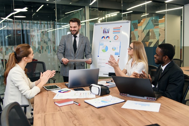 Good-looking high-skilled male business mentor explaining to his attantive business group consist of women and dark-skinned man how they will work together under joint project Premium Photo