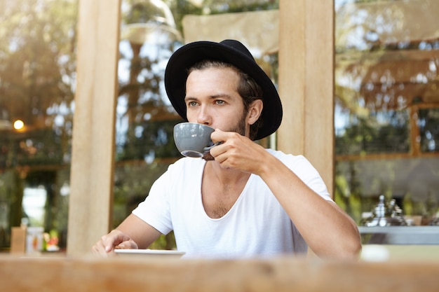 一杯のコーヒーを保持している帽子のかっこいい若い白人男性 無料の写真