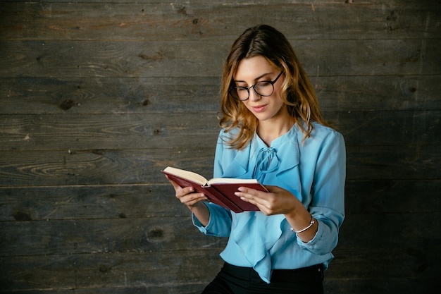 Gorgeous beautiful clever woman in eyeglasses reading interesting book, looks pensive Free Photo