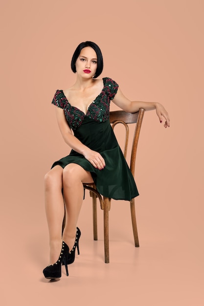 ベージュのスタジオの椅子に座っているショートドレスのゴージャスな女性 プレミアム写真