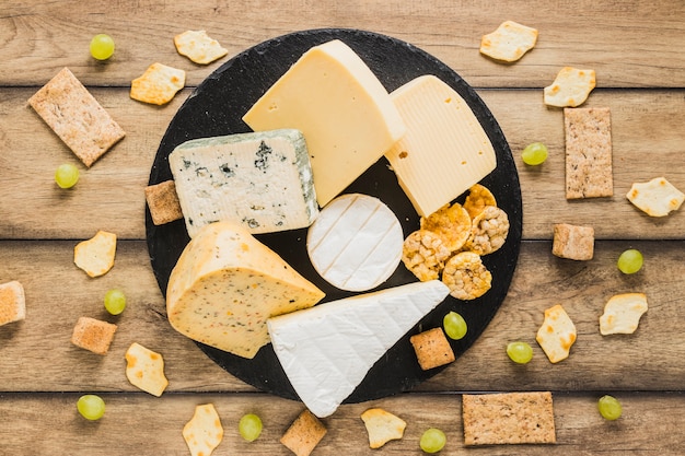 Grapes, cracker, crisp bread and cheese blocks on round slate over the wooden desk Free Photo