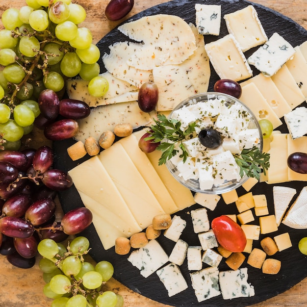 Premium Photo | Grapes with variety of cheese cubes and slices on black ...