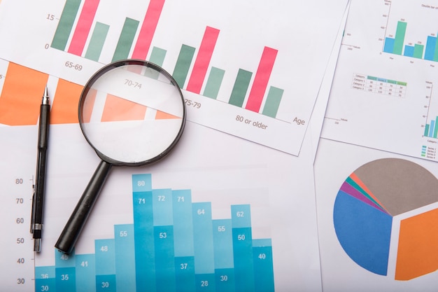 Premium Photo | Graph and pie charts with pen and magnifier