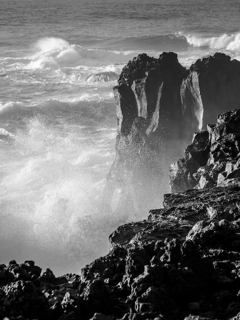 水のしぶきとスプレーで岸の大きな岩に当たる強い波のグレースケールショット 無料の写真