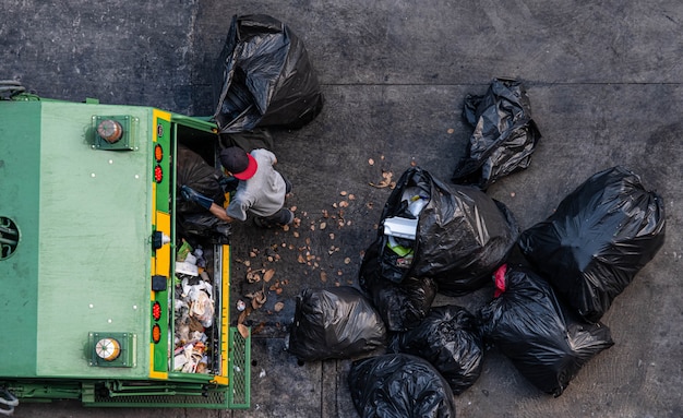 Green garbage truck and the employees are collecting a lot of black garbage bags Premium Photo