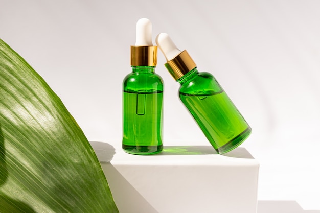 Download Premium Photo Green Glass Cosmetic Bottles With A Dropper On A White Podium With Tropical Leaves