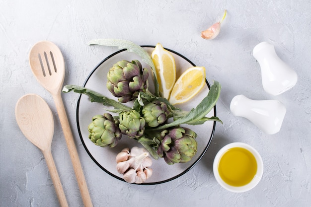 Premium Photo | Green ripe raw artichokes heads ready to cook. artichokes  and ingredients garlic, lemon and olive oil