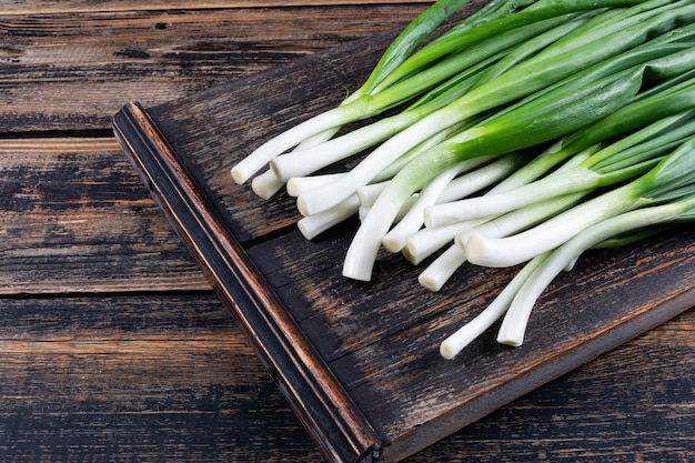 Green spring onions or scallions on a cutting board on a dark wooden table Free Photo