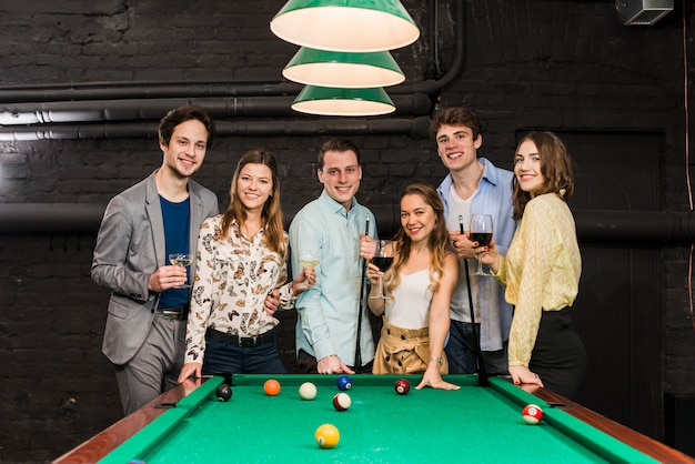 Group of happy smiling friends with drinks standing behind snooker table Free Photo