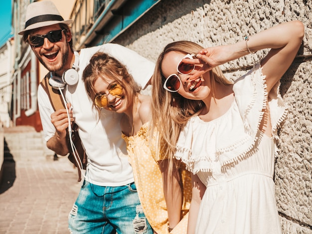 通りでポーズをとる若い3人のスタイリッシュな友人のグループ ファッション男とカジュアルな夏服を着た2人のかわいい 女の子 サングラスで楽しい笑顔のモデル 陽気な女性と屋外の男 無料の写真