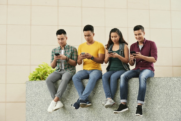 Group of young asian people sitting in street and using smartphones Free Photo