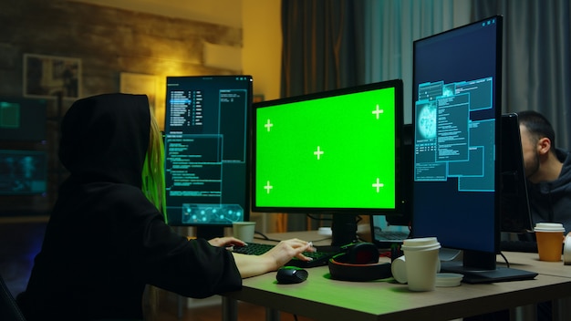 Hacker girl wearing a black hoodie in front of computer with green screen. identity stealing. Free Photo