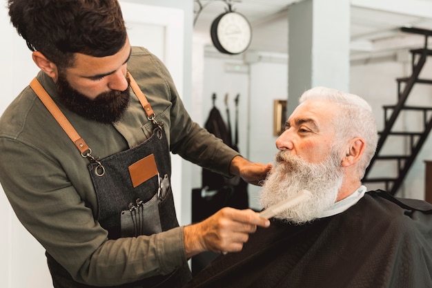 Hairdresser combing beard of aged client in barbershop Free Photo