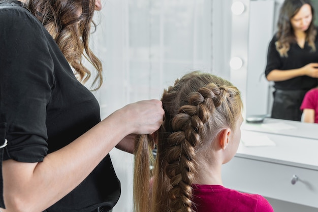 Premium Photo Hairdresser Weaves A Braid To A Preteen Blond Girl In A Beauty And Hair Salon