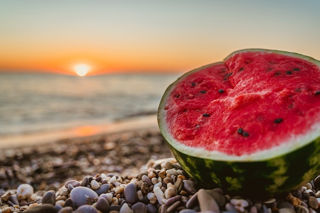 Premium Photo | Half a watermelon on the beach with pebbles at sunset ...