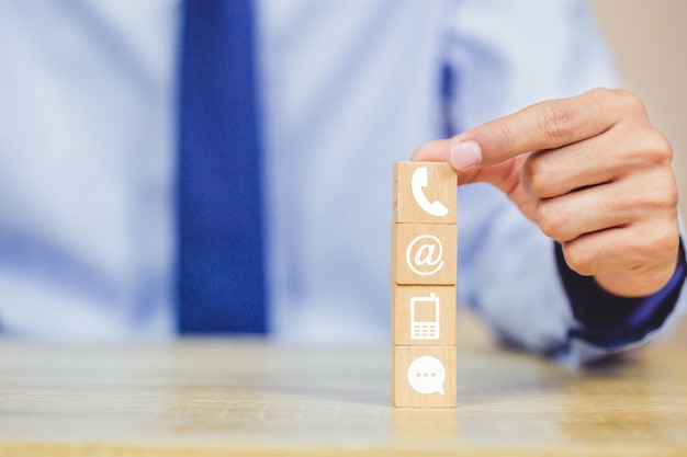 Hand arranging wood block stacking with iconl telephone, mail, address and mobile phone Premium Photo