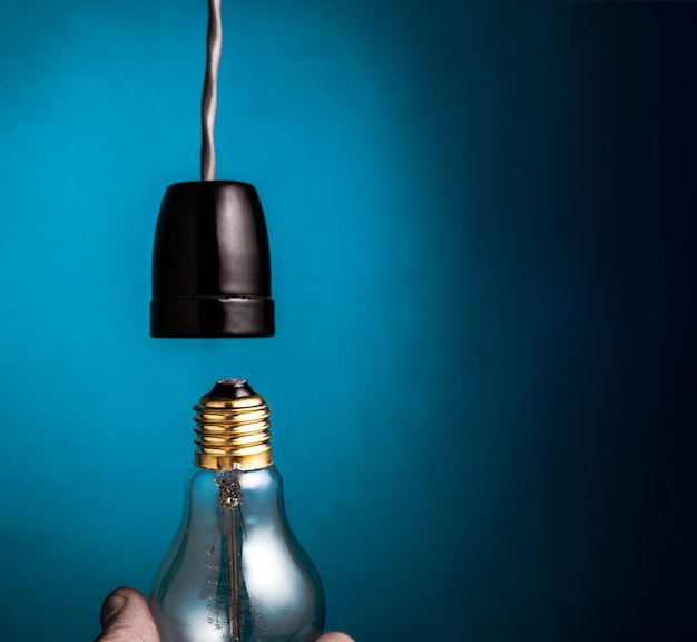 Hand changing a antique edison style filament light bulbs on dark blue background. Premium Photo