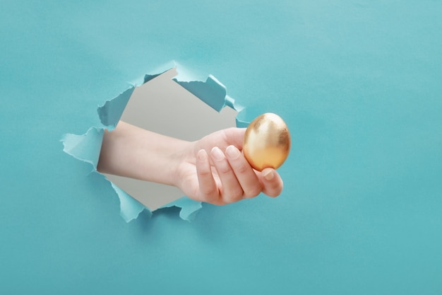 Hand gives golden egg through paper hole Premium Photo