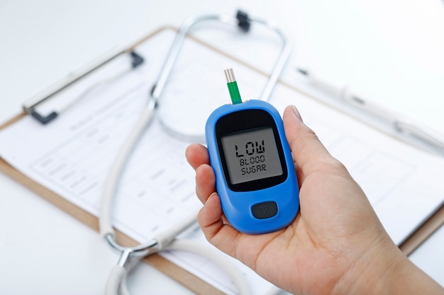 Hand holding a blood glucose meter measuring blood sugar, the background is a stethoscope and chart file Free Photo Hand holding a blood glucose meter measuring blood sugar, the background is a stethoscope and chart file Free Photo