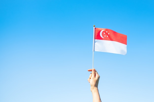 Premium Photo Hand Holding Singapore Flag On Blue Sky Background Singapore National Day And Happy Celebration Concepts