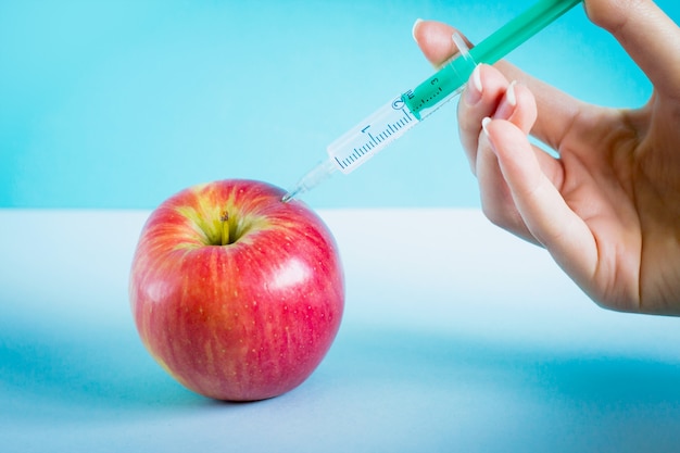 Hand makes gmo injection into an apple. gmo concept with apple; World Food Safety Day